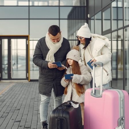 Family standing outdoors with luggage and checking passports Family of three going on vacation. Man and woman cheching their passports. Mother, father and daughter wearing warm clothes.